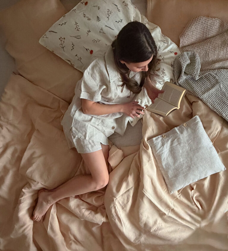 Štýlovo ustlaná posteľ s vrstvením marhuľových obliečok Adela, prúžkovaných vankúšov a vaflového plédu.